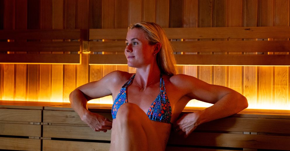 Woman in a blue patterned bikini relaxing inside a wooden sauna, wondering how often should you use infrared saunas.