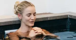 A woman sits in a hot tub, hands clasped, enjoying relaxation, with a focus on the benefits of ice baths.