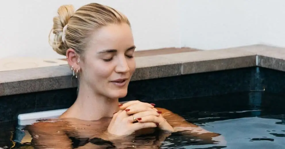 A woman sits in a hot tub, hands clasped, enjoying relaxation, with a focus on the benefits of ice baths.