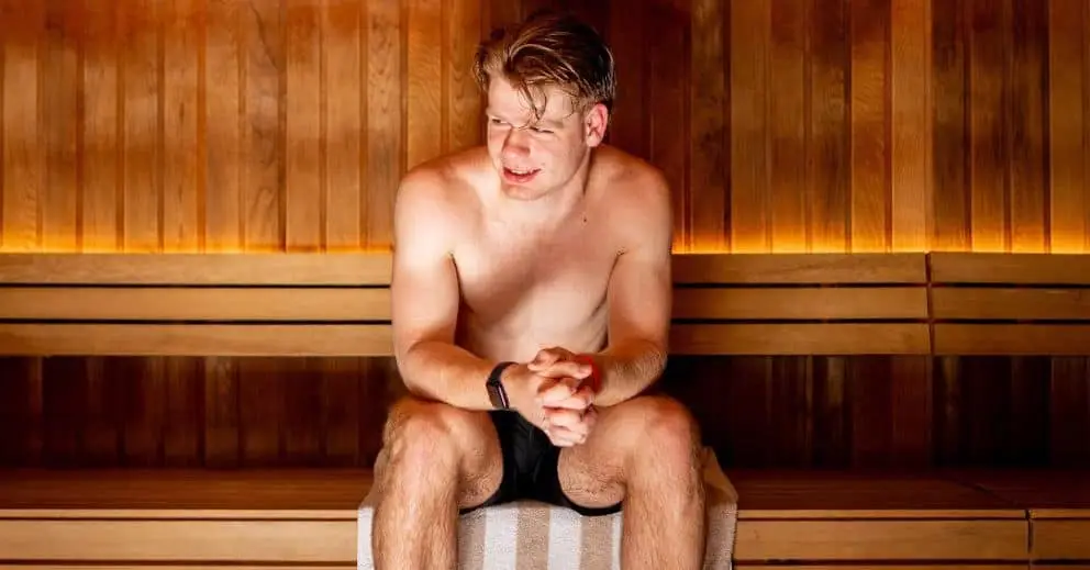A man sits in a traditional sauna, hands on knees, enjoying the heat for skin health benefits.