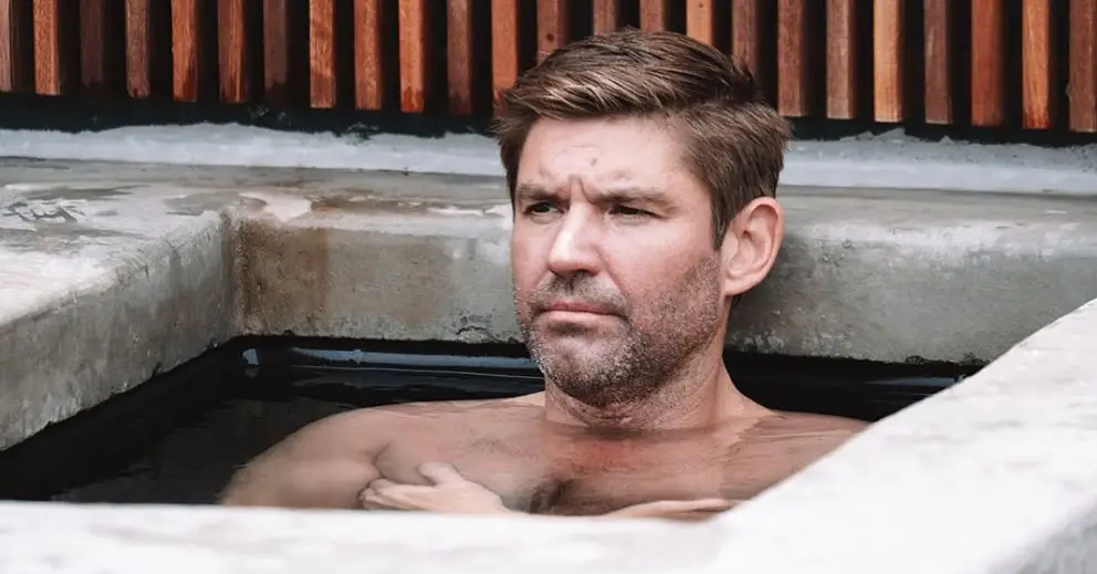 A shirtless man sits in an ice bath, representing Brisbane locals' wellness routine of ice baths paired with sauna sessions.