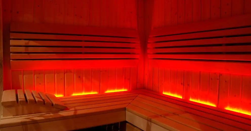 Wooden infrared sauna interior with bench seating and red ambient lighting.