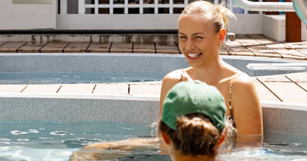A woman smiling at another in a pool, highlighting the bathhouse vs spa experience.