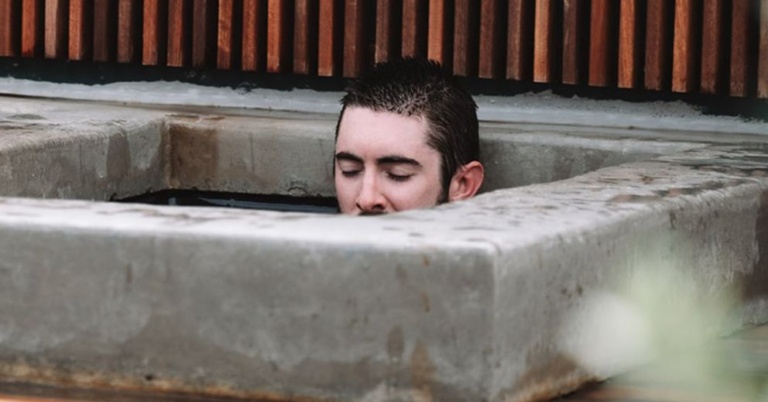 Person with closed eyes in a concrete tub, practicing cold exposure to ease anxiety.