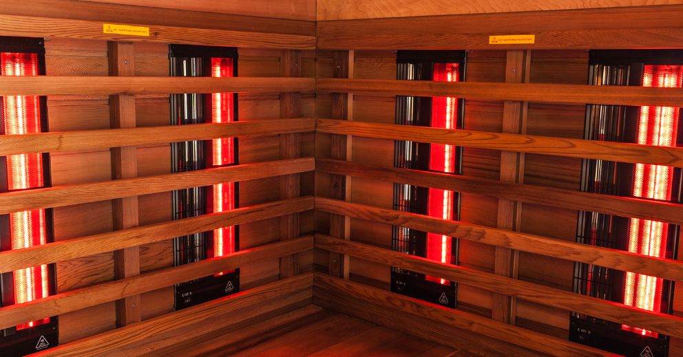 Wooden infrared sauna for older adults with red heaters lining the interior corner walls.