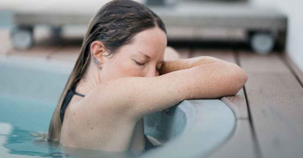 Person enjoying post-gym recovery, resting arms and head on pool edge, eyes closed, partially submerged.