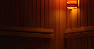 Dimly lit wooden sauna interior with a glowing wall lamp for a nervous system reset.