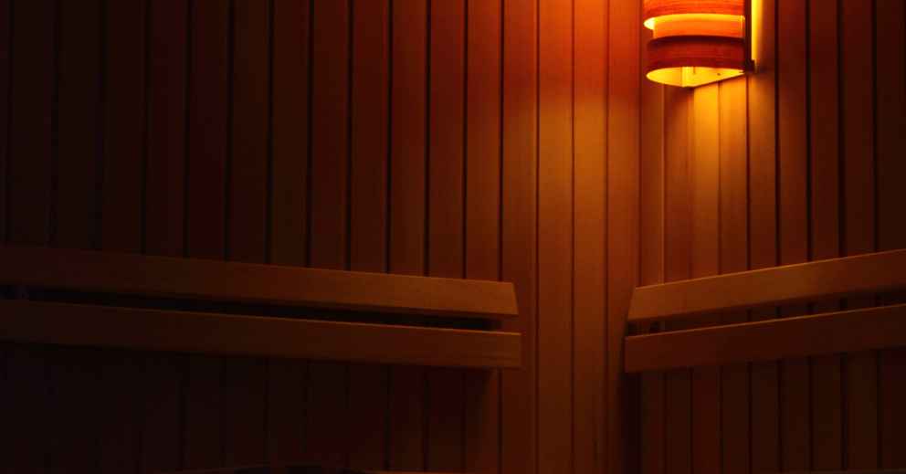 Dimly lit wooden sauna interior with a glowing wall lamp for a nervous system reset.
