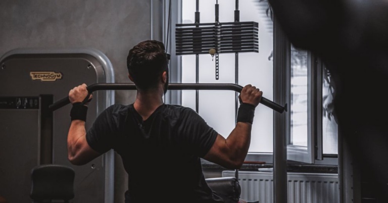 Person using a lat pulldown machine in a gym, benefits from ice baths for strength training.