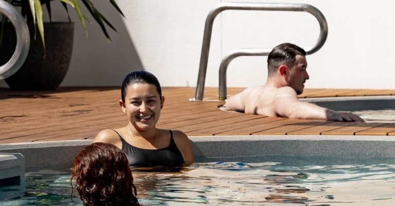 Two people are relaxing in a pool, balancing recovery vs relaxation as a man sits poolside.