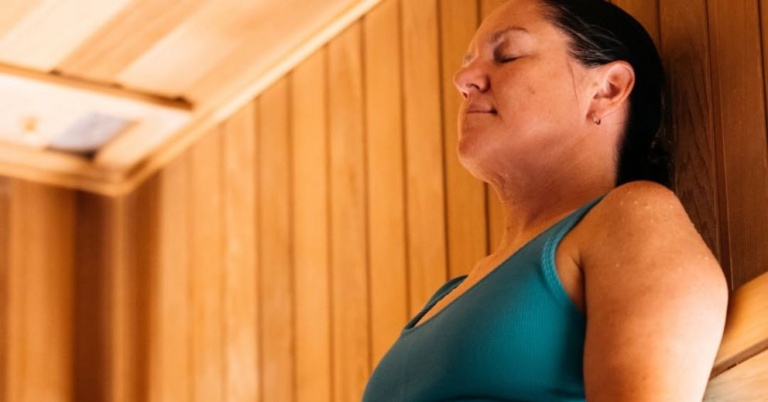 Woman in a blue top relaxes in a wooden sauna, ideal as a sauna for desk workers.