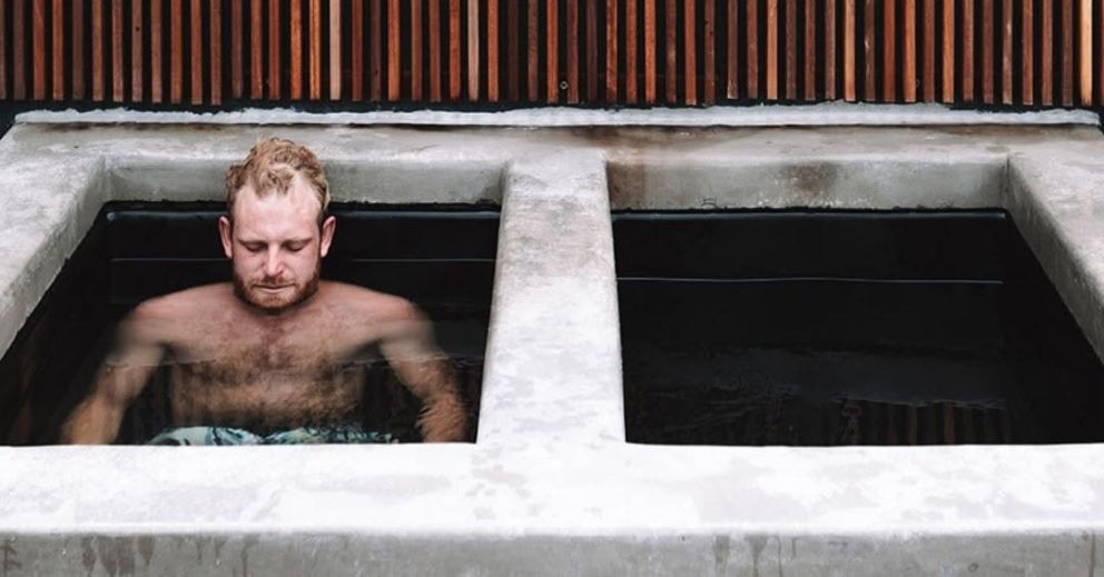 A man sits chest-deep in a concrete bath filled with water, highlighting ice bath safety measures.