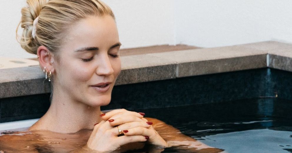 Woman with closed eyes relaxes in a tiled indoor pool, hands clasped together after ice baths.