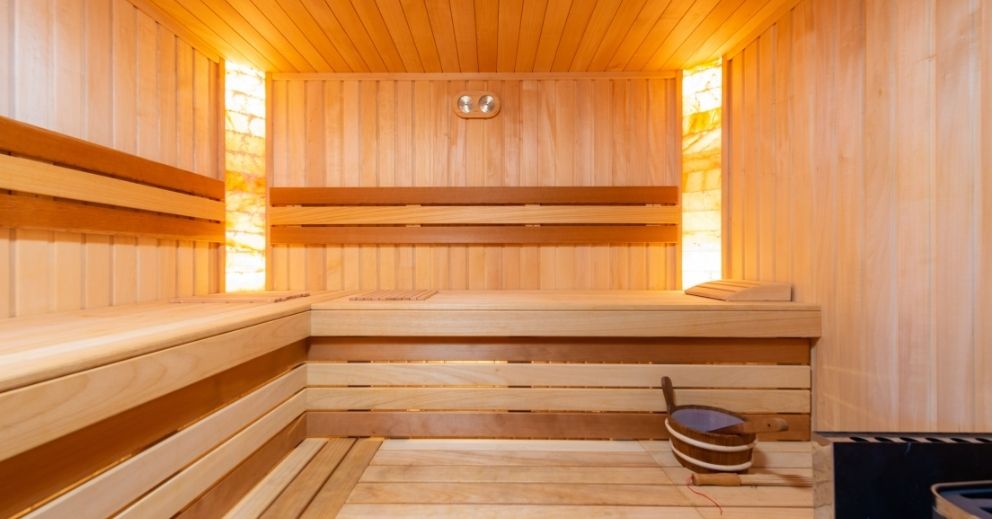 Wooden sauna with tiered benches, a bucket, and integrated lighting for a relaxing night routine.